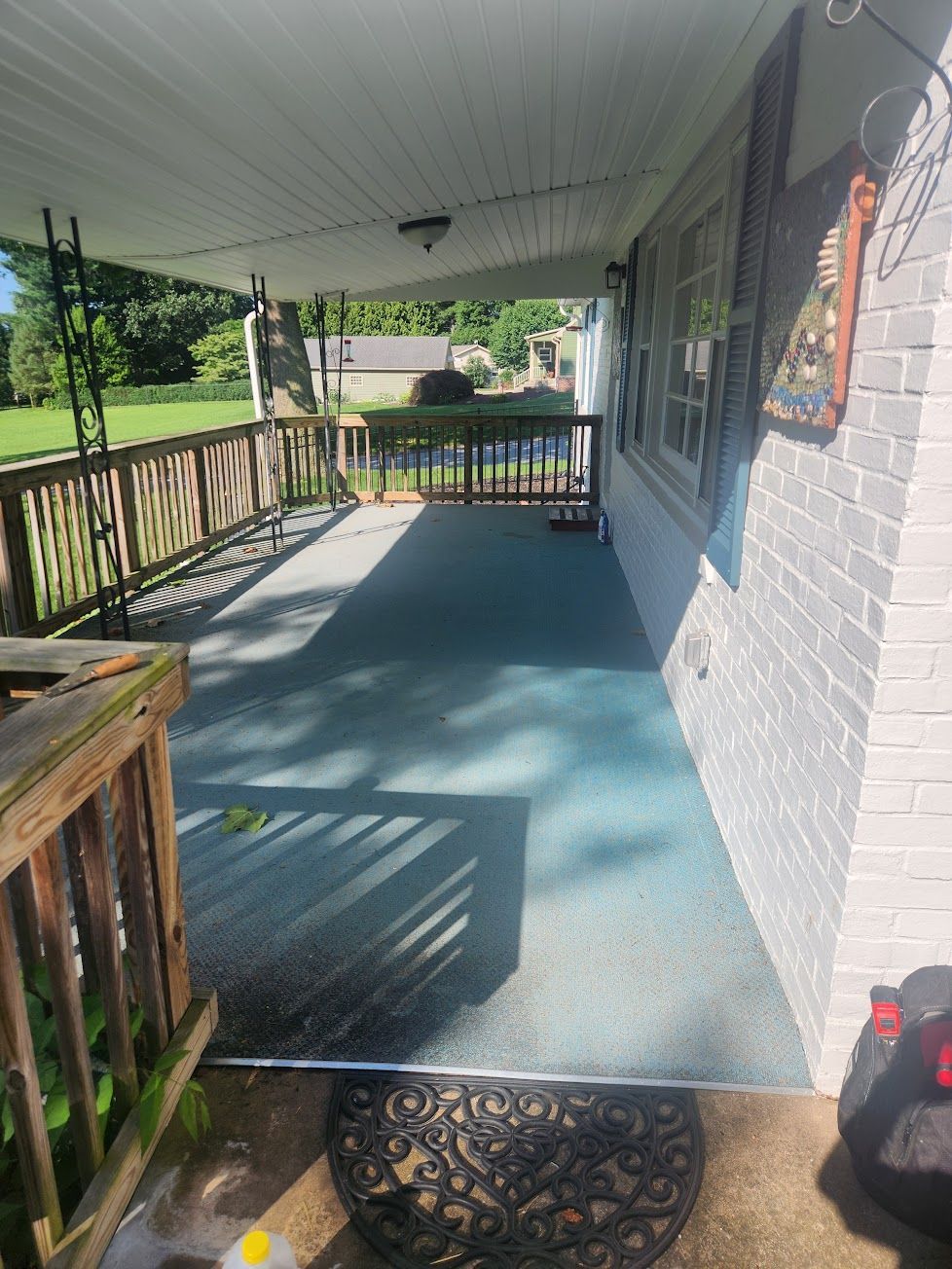 A covered porch with a textured, blue-grey surface, wooden railings, and a white brick house wall.