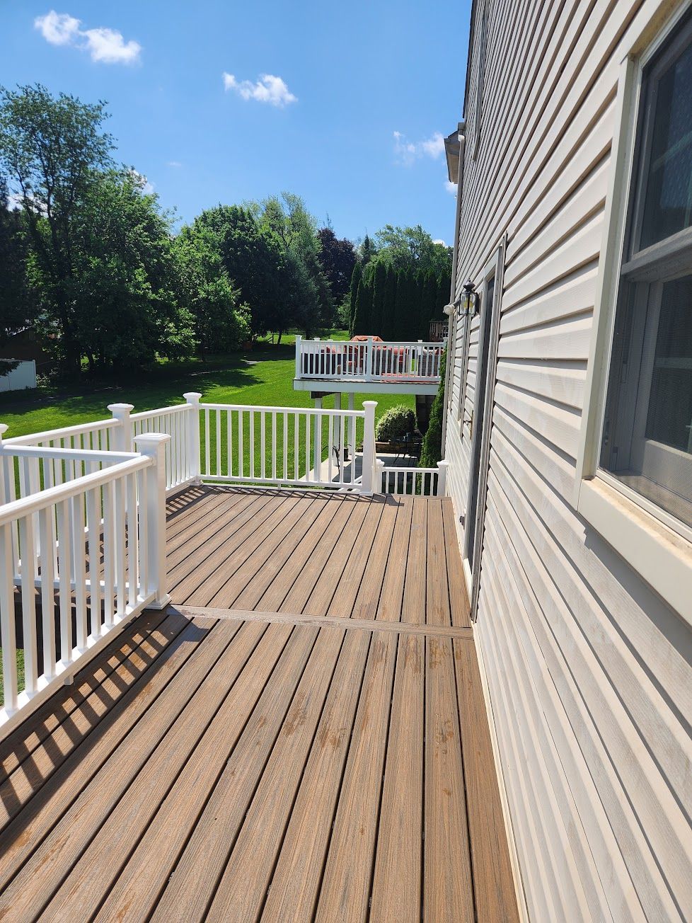 A wooden deck with white railings extending from a house with beige siding, overlooking a green backyard on a sunny day.