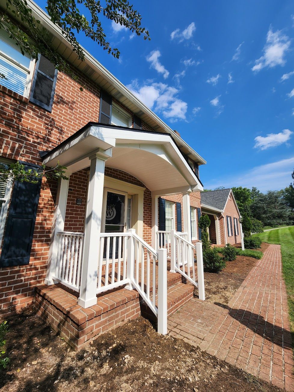 A brick home featuring a white-pillared front porch and walkway under a clear blue sky.