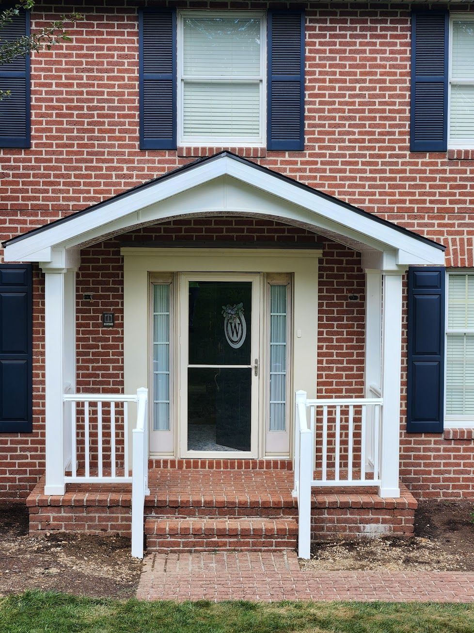Front exterior of a brick house featuring a covered porch, white railings, a front door with sidelights, and blue shutters.