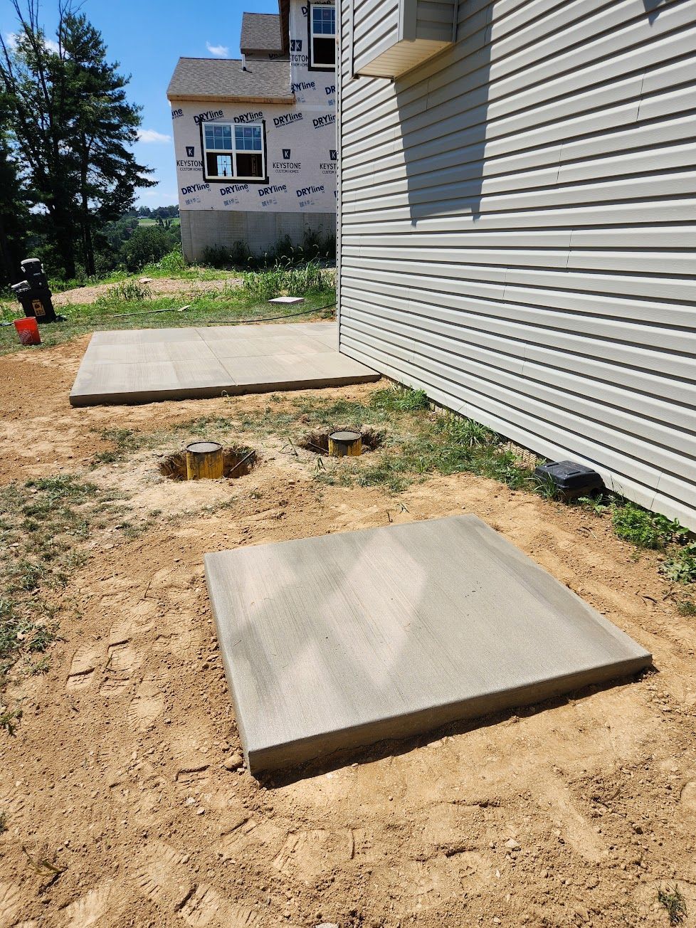 A house under construction with two new concrete pads and two pier holes in a grassy backyard.