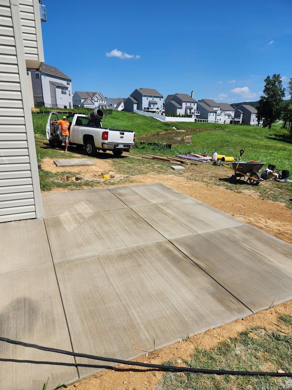A white pickup truck parked on a lawn next to a concrete patio behind a house in a residential neighborhood.