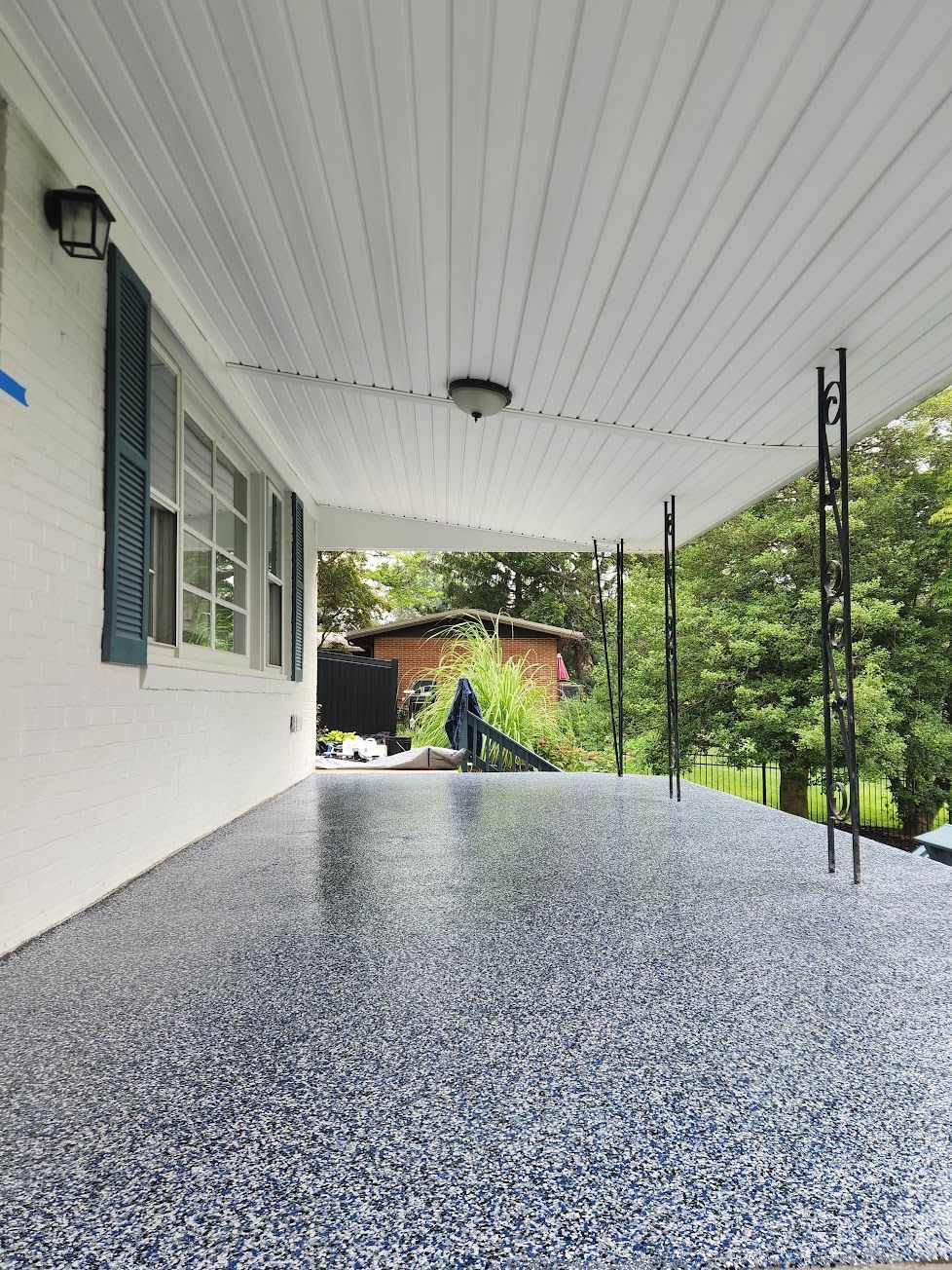 A porch with a fresh blue and white speckled epoxy floor, white siding, blue shutters, and a white beadboard ceiling.