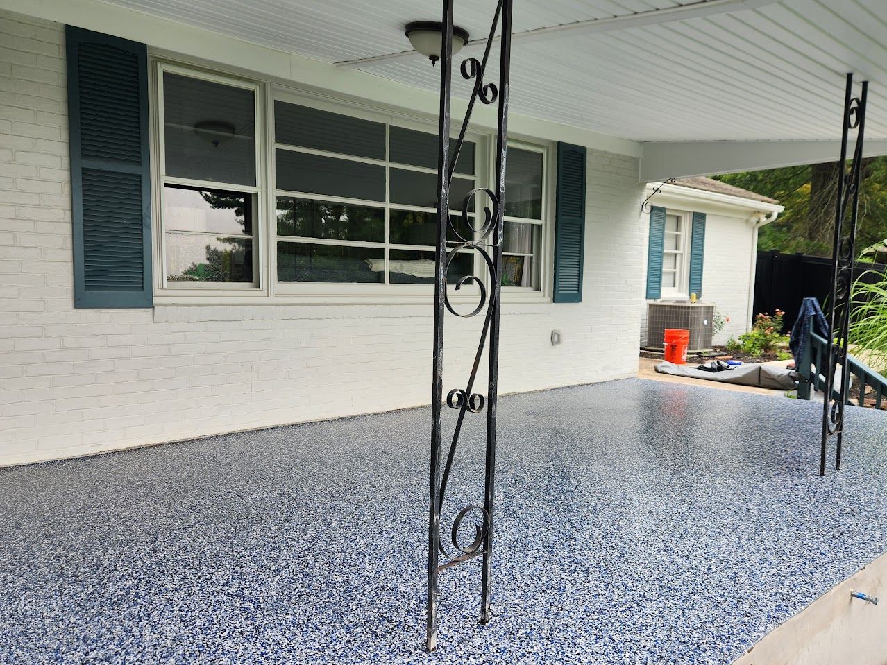 A white brick house with blue shutters, a covered porch, and a freshly applied speckled gray epoxy floor coating.