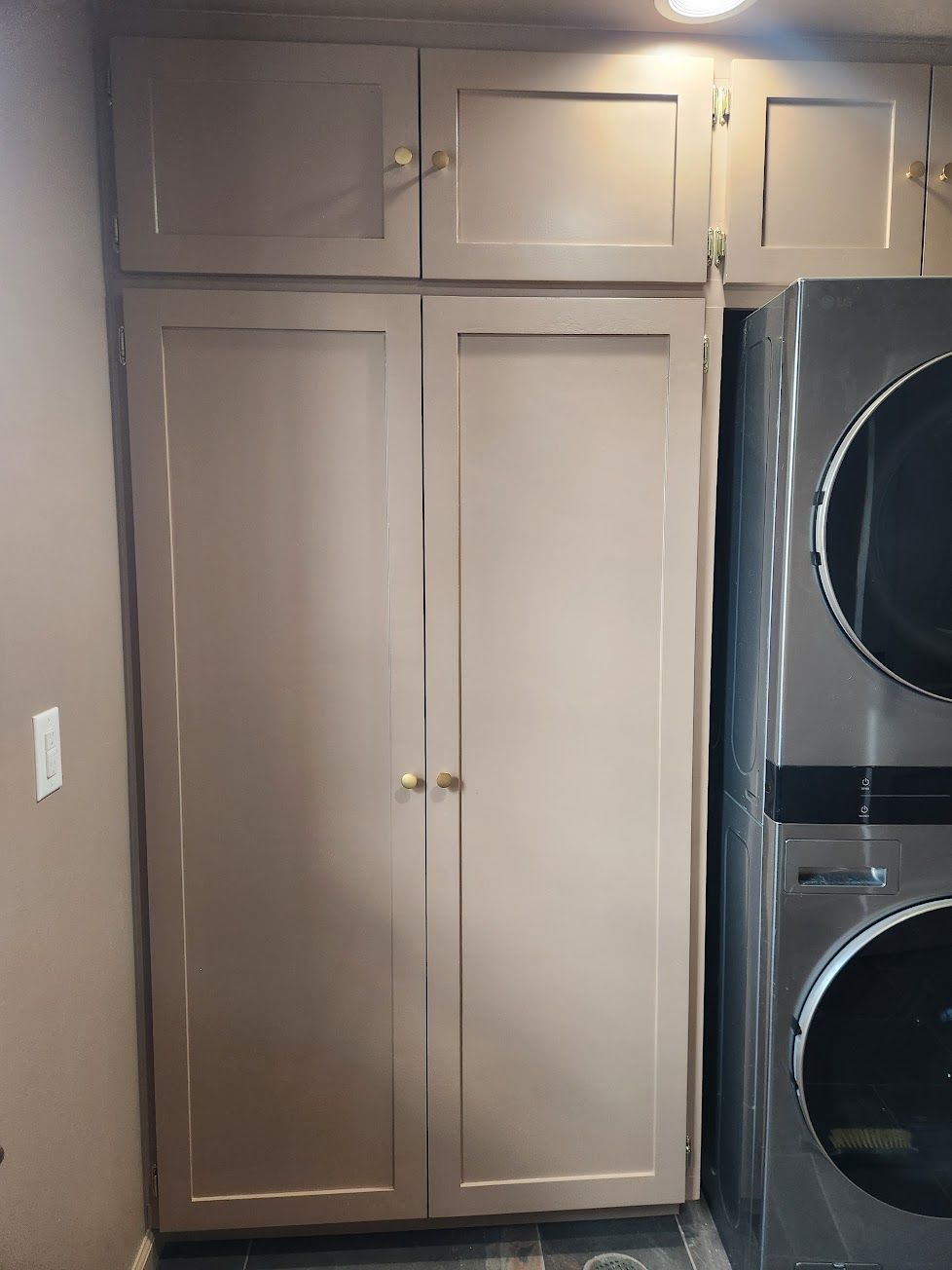 Taupe kitchen cabinets with gold hardware next to a stacked washer and dryer unit.