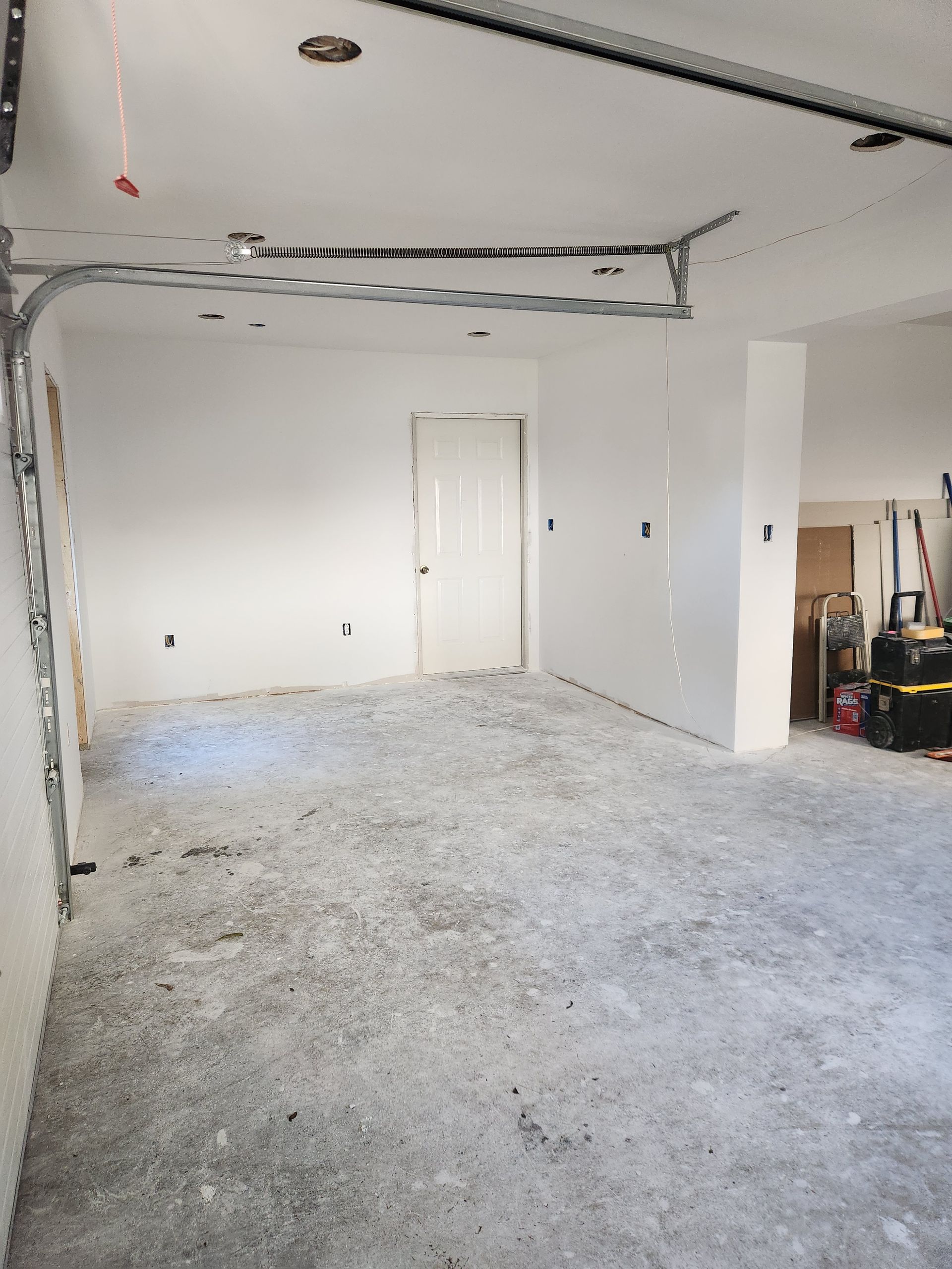 An unfinished garage with white walls, a single door, and a raw concrete floor.