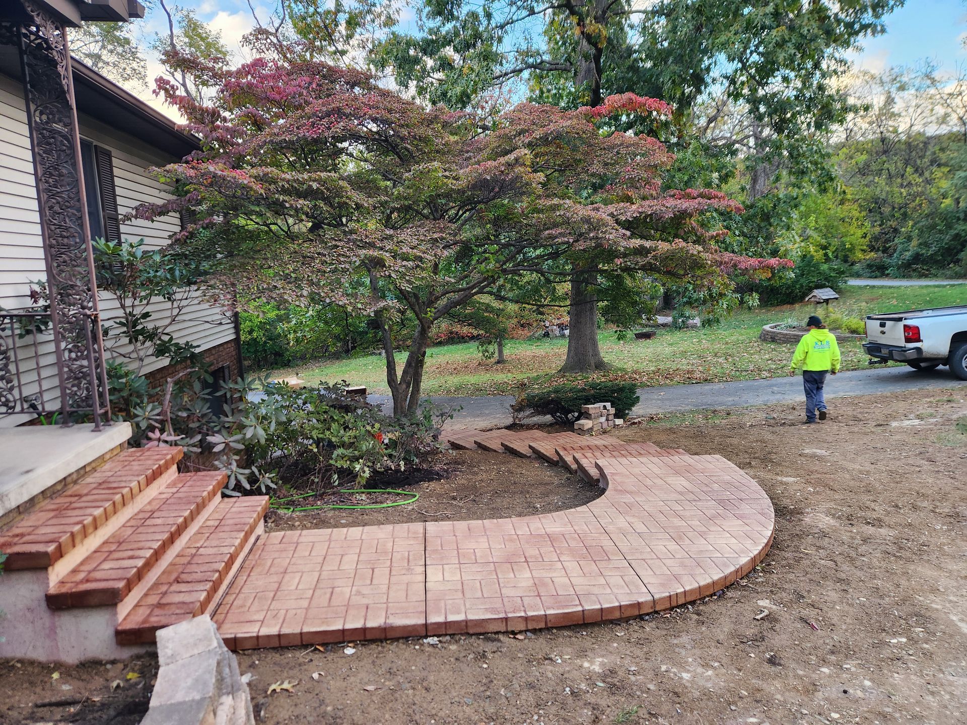 Newly installed curved brick walkway and steps leading to a house entrance, with a worker in the background.