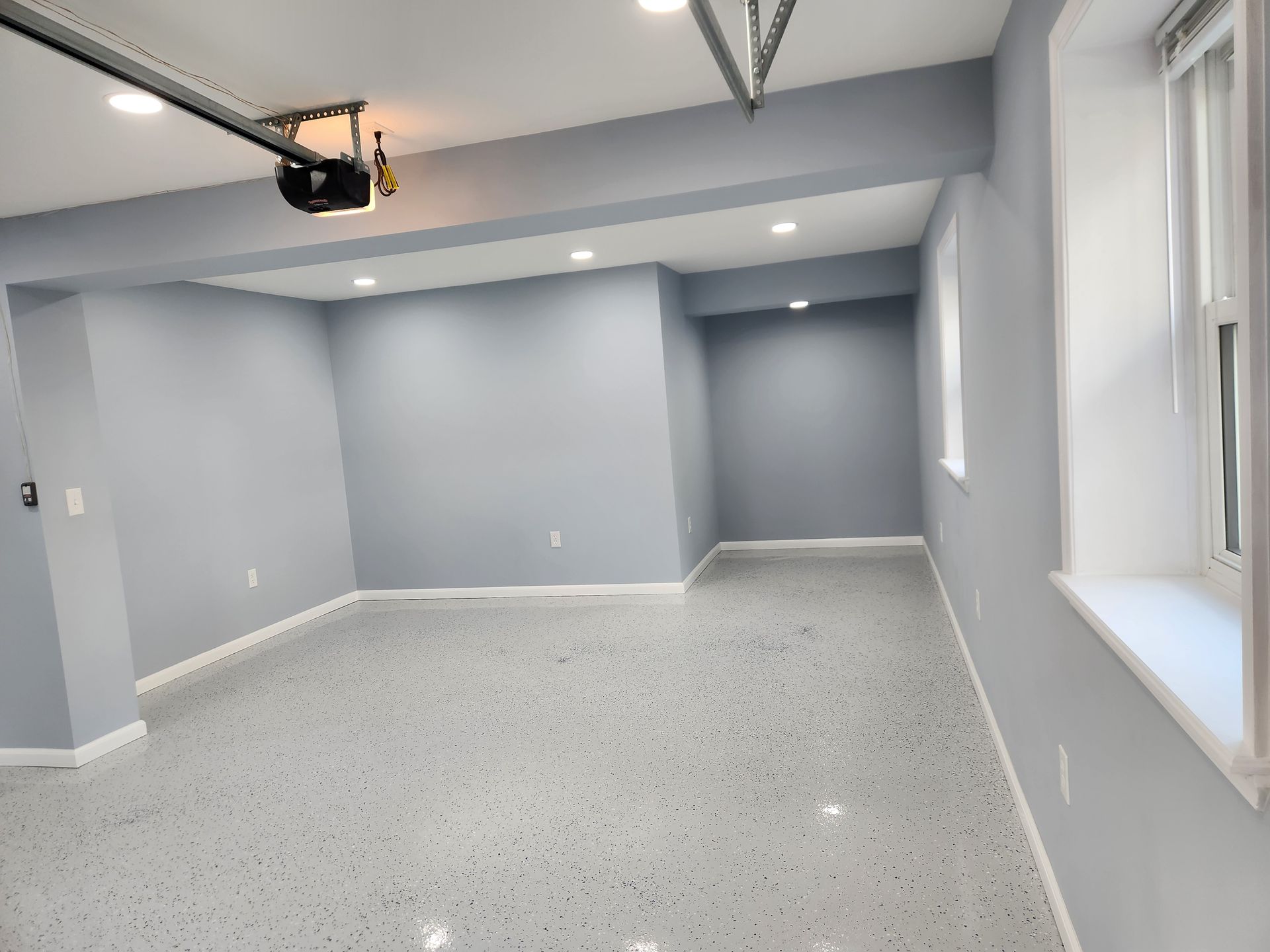 A finished garage interior with light grey walls, white trim, recessed lighting, and a grey speckled epoxy floor.