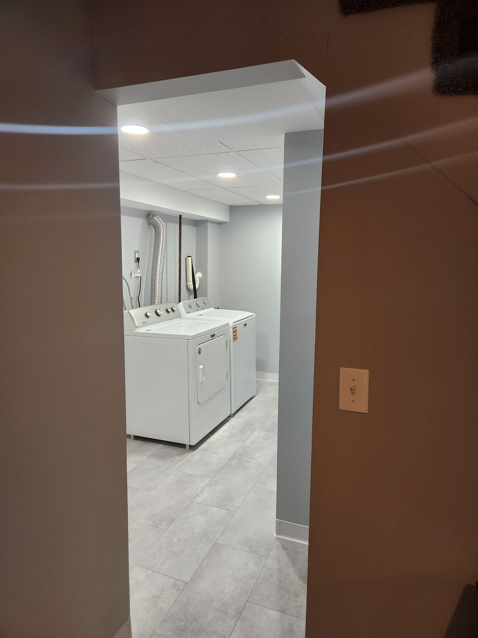 A view through a doorway into a laundry room with white appliances and light gray flooring.