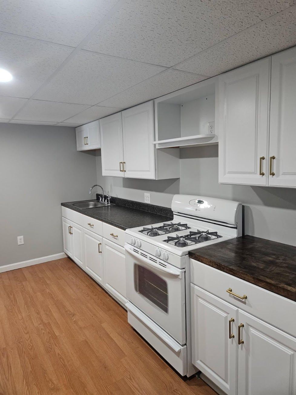 A small kitchen with white cabinets, dark countertops, a white gas stove, and light wood flooring.