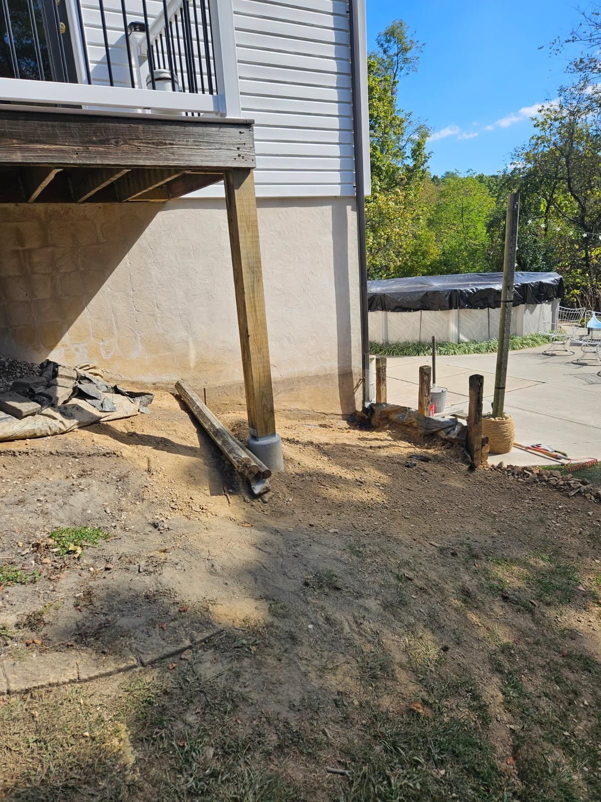 A side view of a house deck with exposed wooden support posts and a pile of dirt and debris on the ground below.