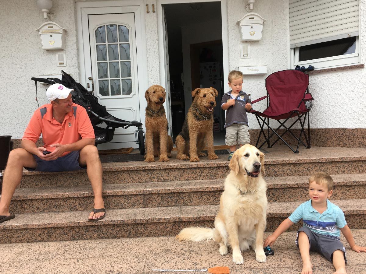 Family and two dogs sitting on front steps of a house, with a child in a red chair on the porch