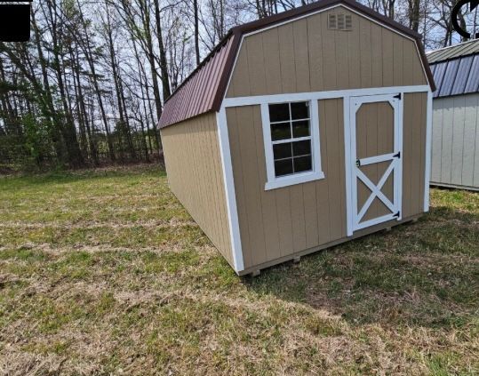 Tan shed with white trim, a brown roof, and a window and door in a grassy yard.