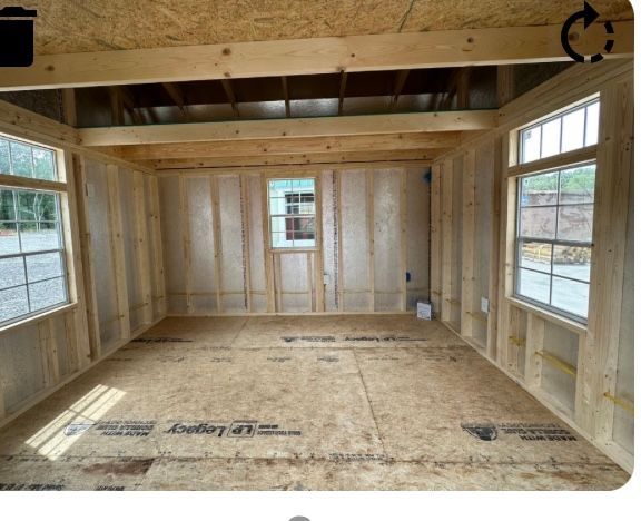 Interior view of a shed under construction. The unfinished space has wooden framing, OSB walls, and windows.