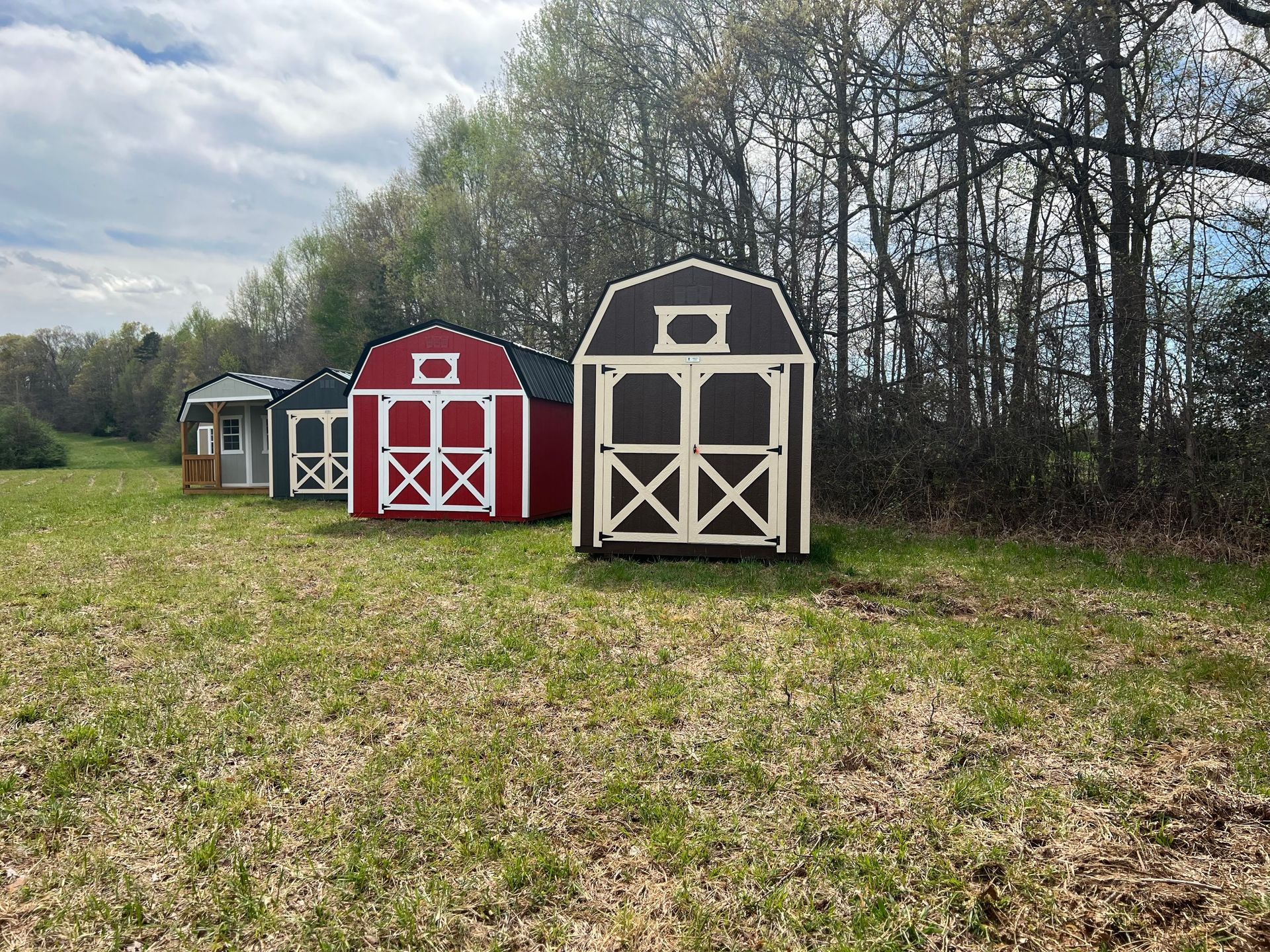Three colorful sheds of varying sizes stand in a grassy field, with a forest in the background.