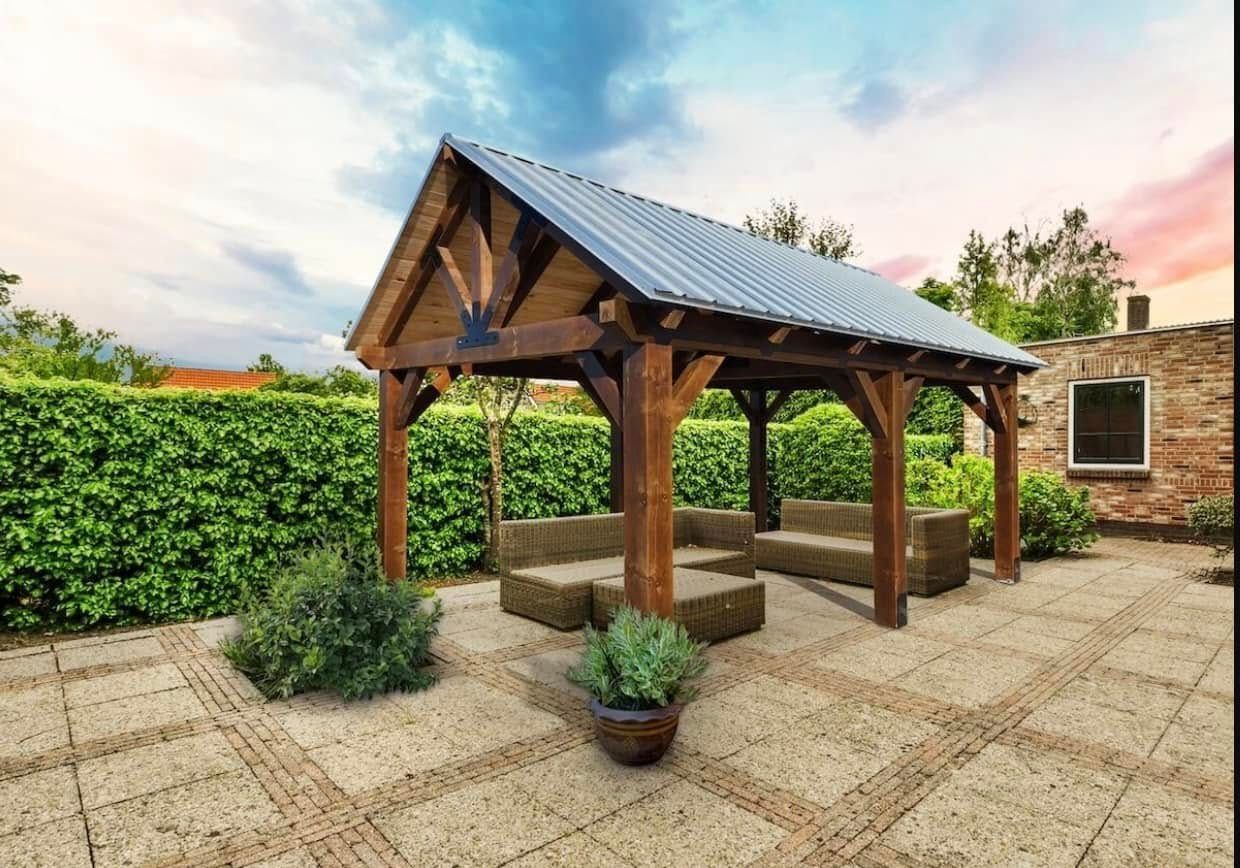 Wooden gazebo with metal roof on a stone patio. Two seating areas made of hay bales are inside
