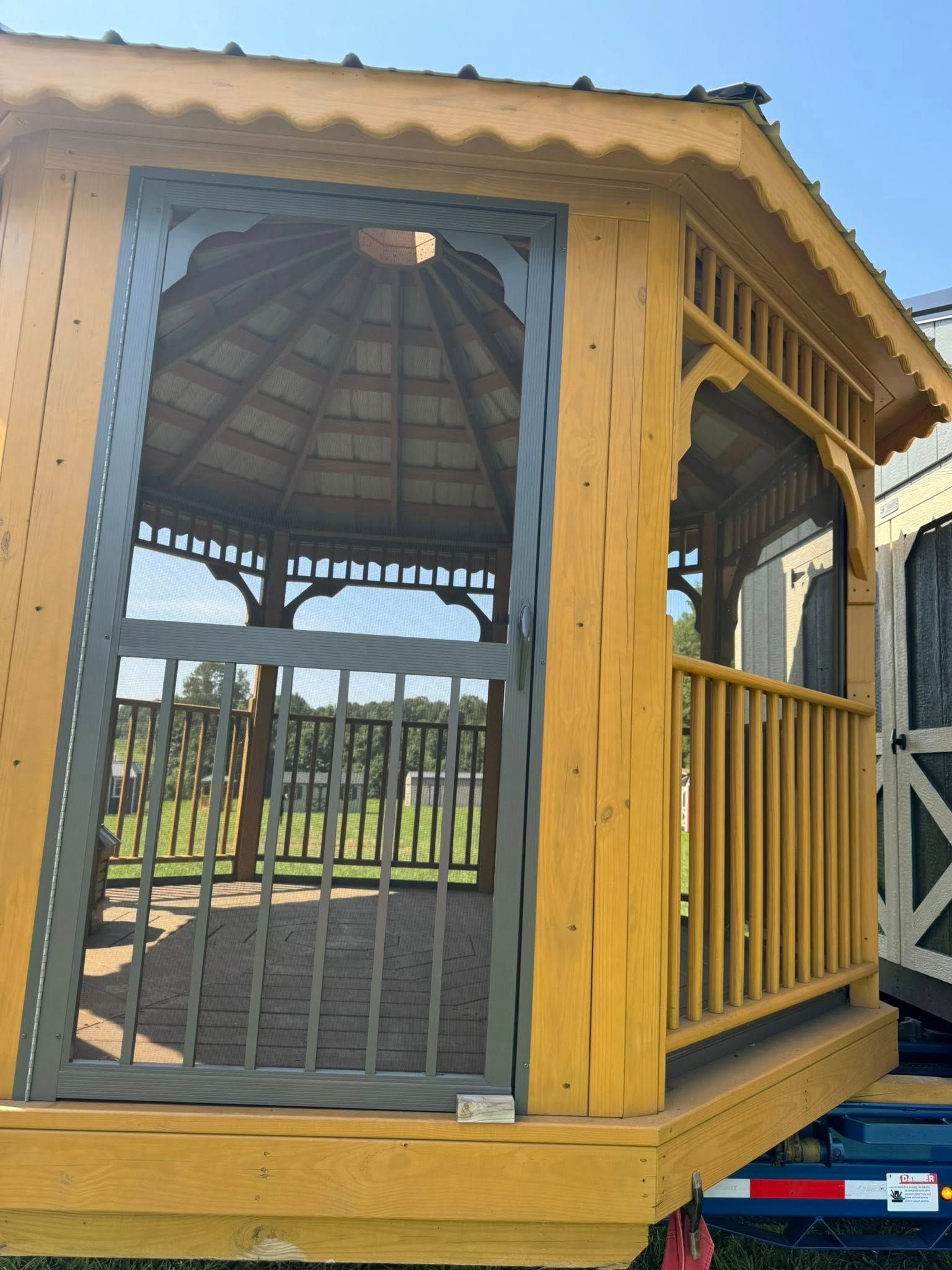 A wooden gazebo with a gray door and railing, set on a wooden deck.