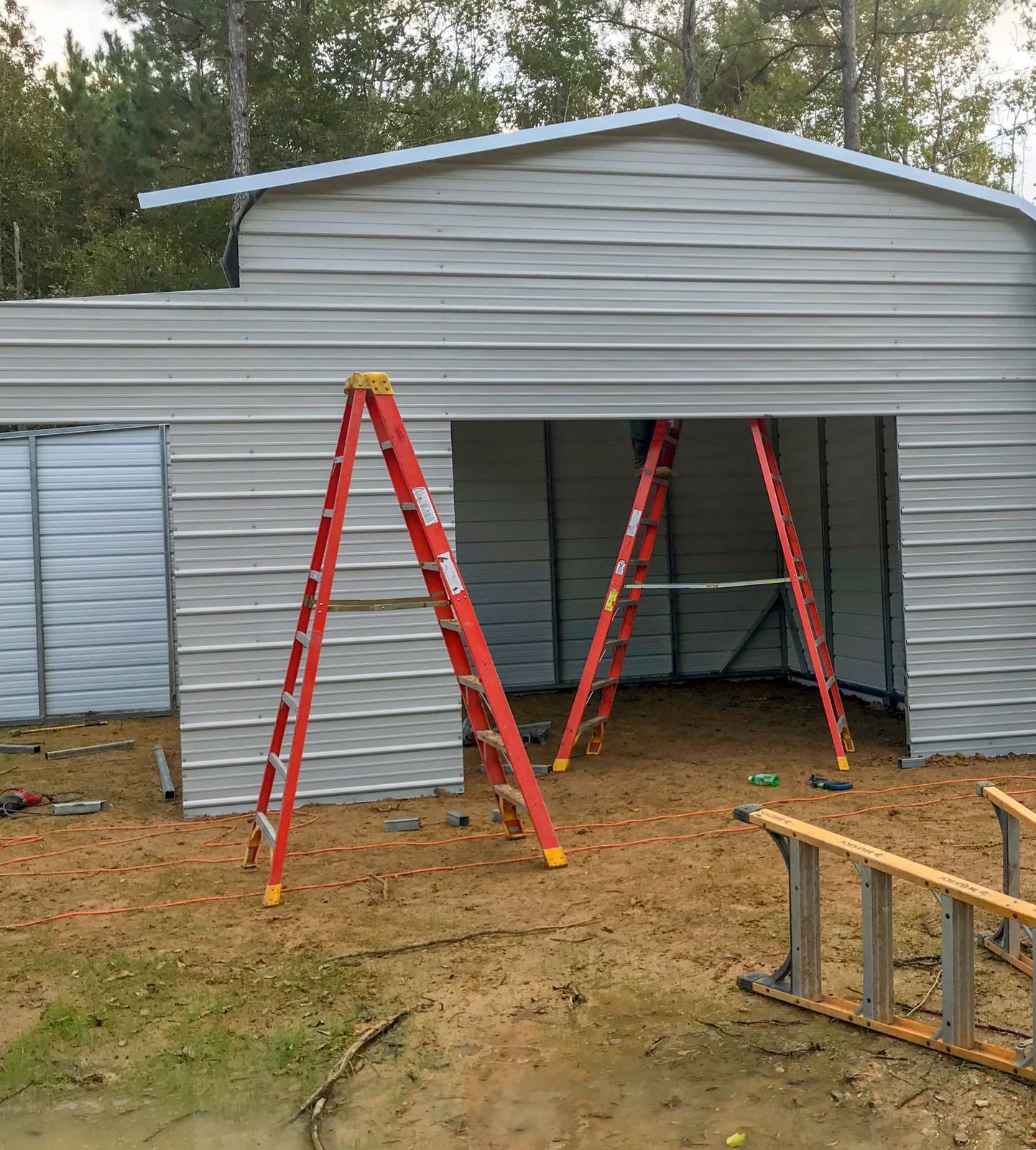 Front of a gray house under renovation with red ladders and a wooden sawhorse in front of the open entrance
