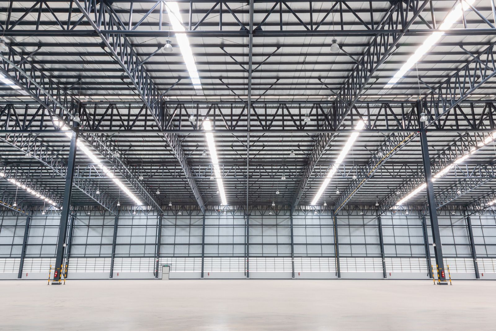 Empty industrial warehouse with high steel trusses and bright overhead lights