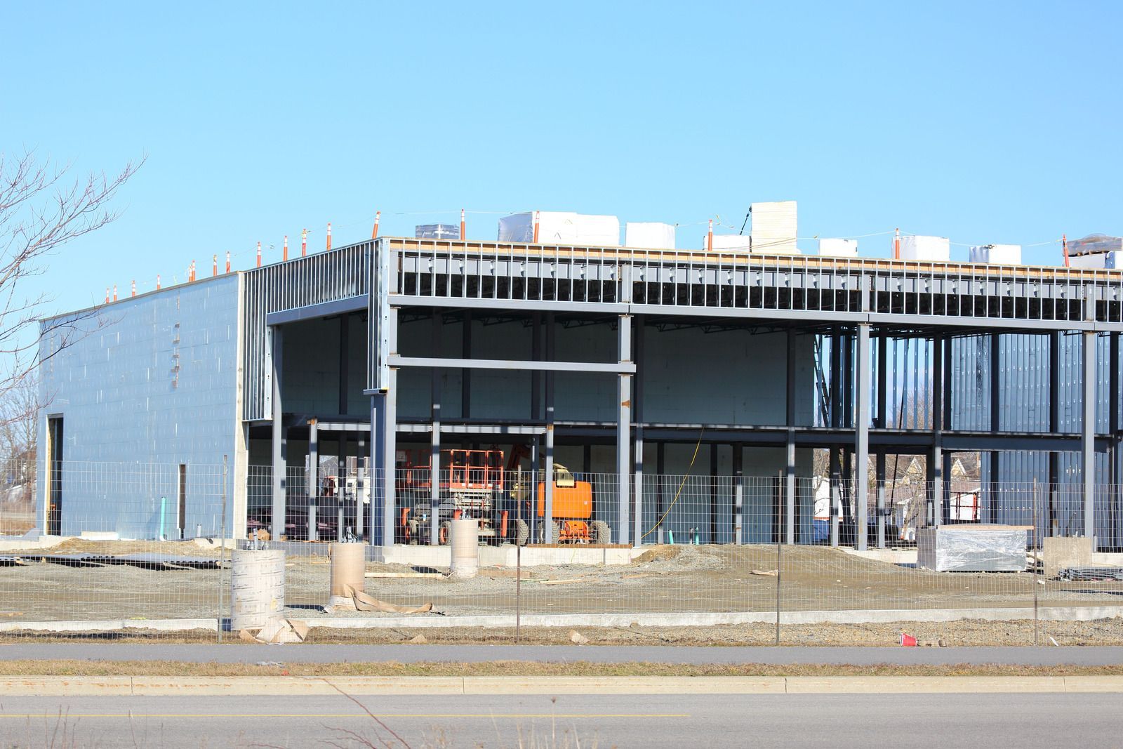 Partially constructed commercial building with steel frame and orange machinery behind a roadside fence