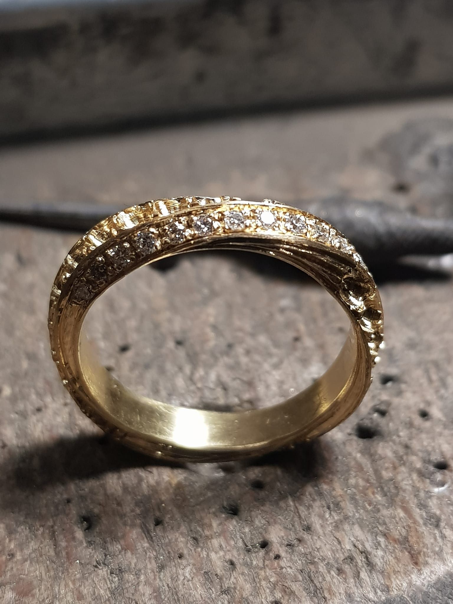 Anello in oro con fascia testurizzata e piccole pietre preziose, su una superficie testurizzata.