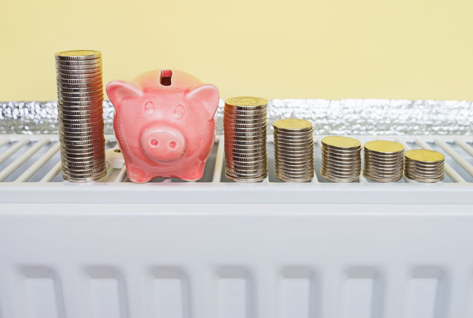 Pink piggy bank and diminishing coin stacks on a radiator, symbolizing decreasing savings.