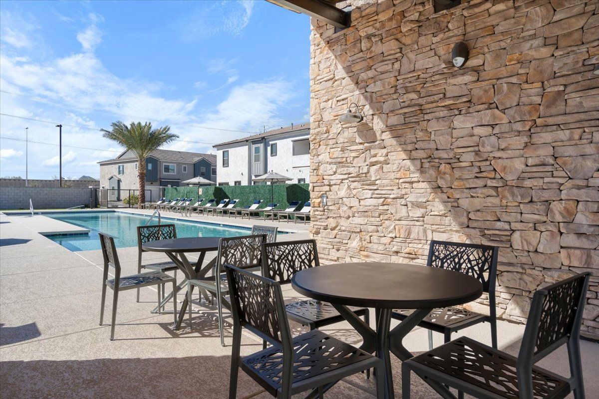 A patio area with tables and chairs next to a swimming pool.