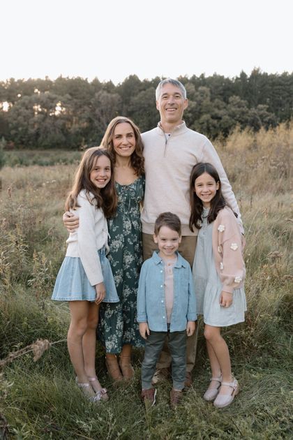 Four children posing together in a grassy field at sunset, with trees in the background.
