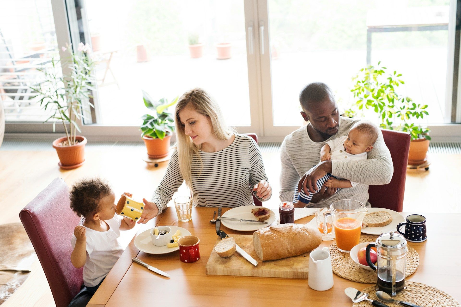 Family sharing breakfast at a bright kitchen table with bread, fruit, and coffee