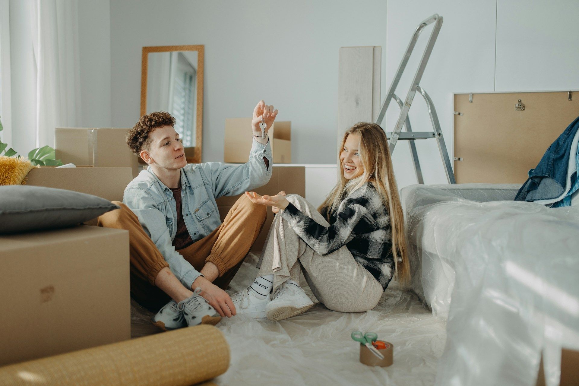Two people sitting on the floor in a bright room, toasting drinks amid unpacked moving boxes