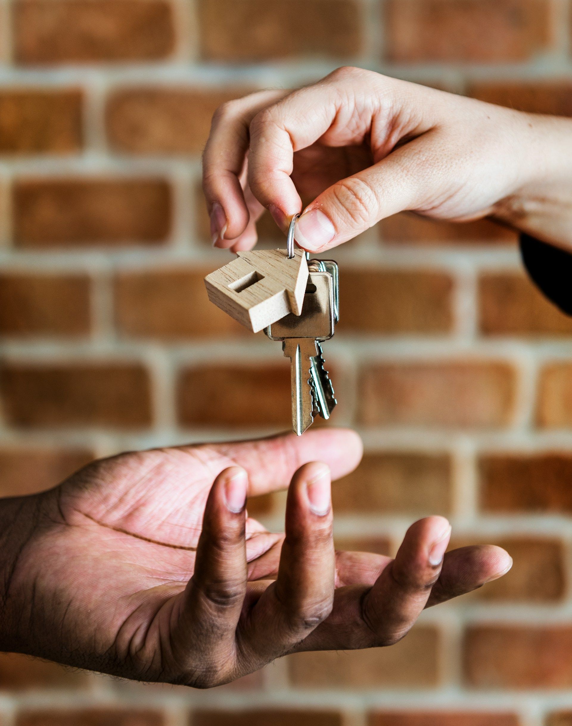 Handing over a house key between two hands against a brick wall background