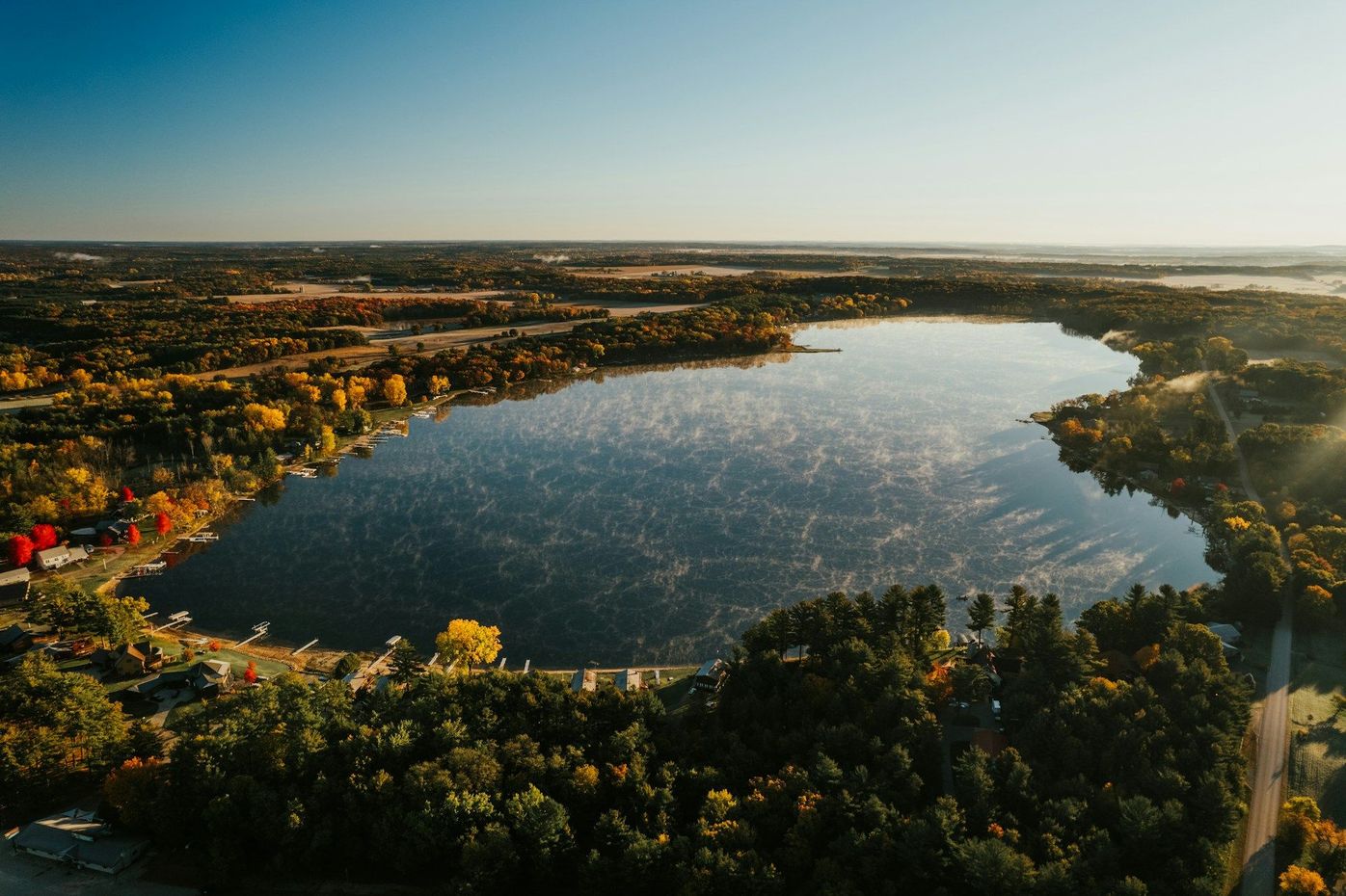 Aerial view of a large lake surrounded by trees and city buildings at sunset