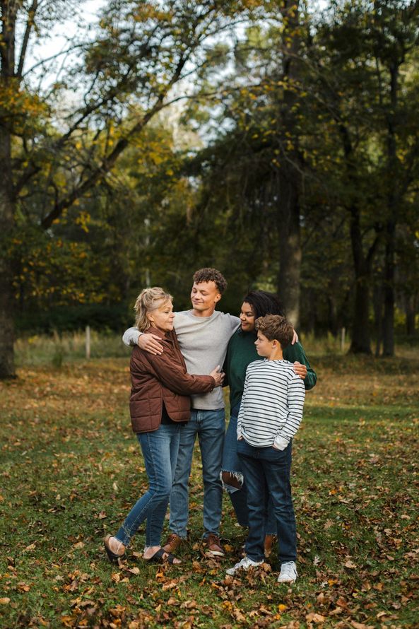 Four people standing together in a park, smiling and hugging in autumn leaves.