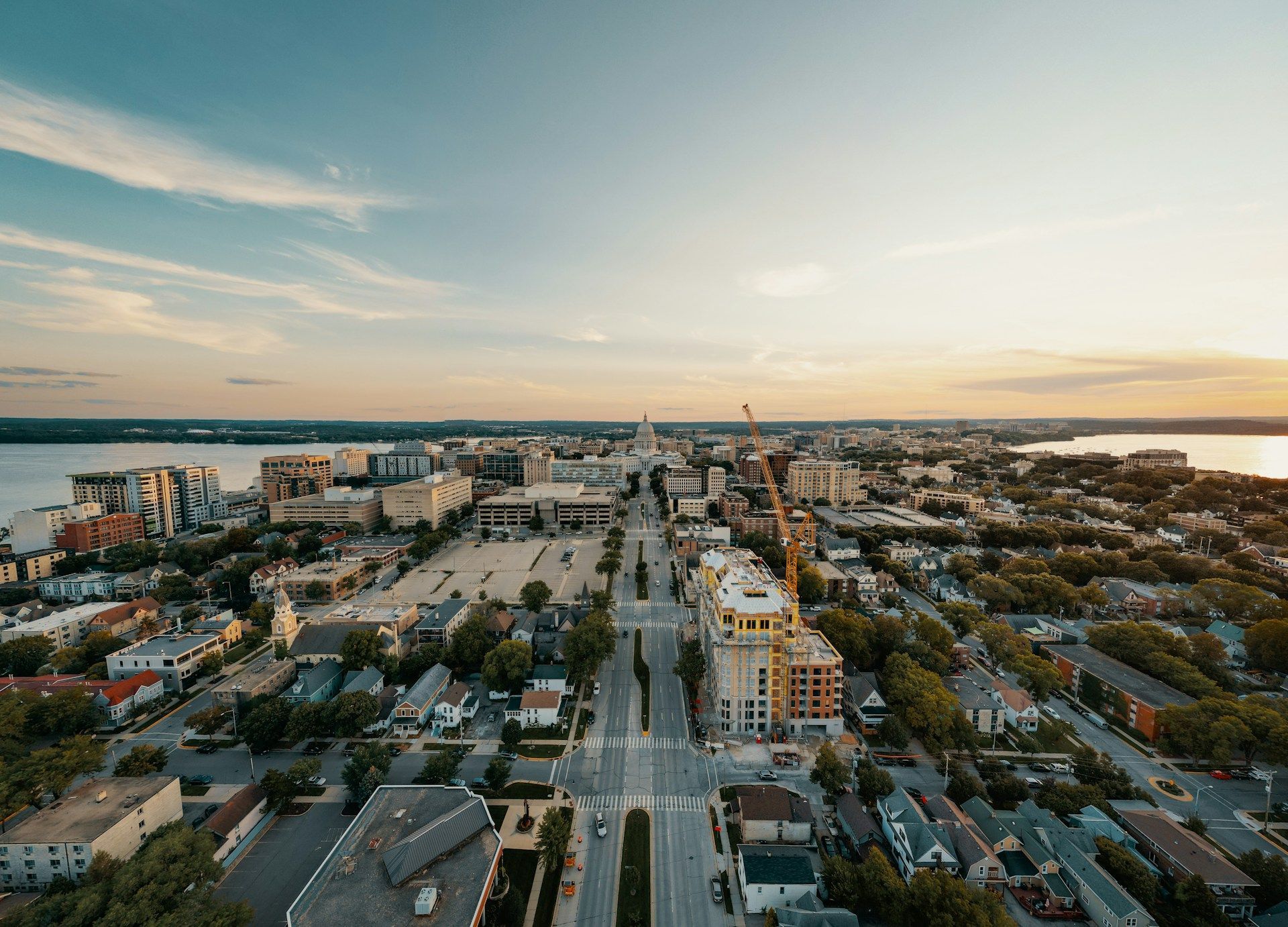 Aerial view of a coastal city at sunset with roads, buildings, and water in the distance