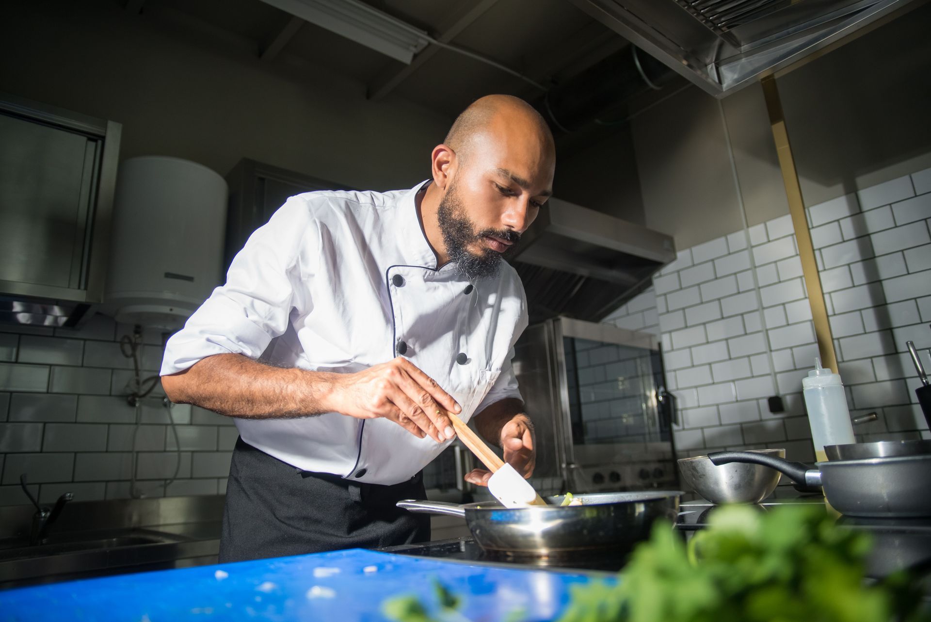 Chef plating food in a stainless-steel kitchen, focused on cooking over a stovetop.