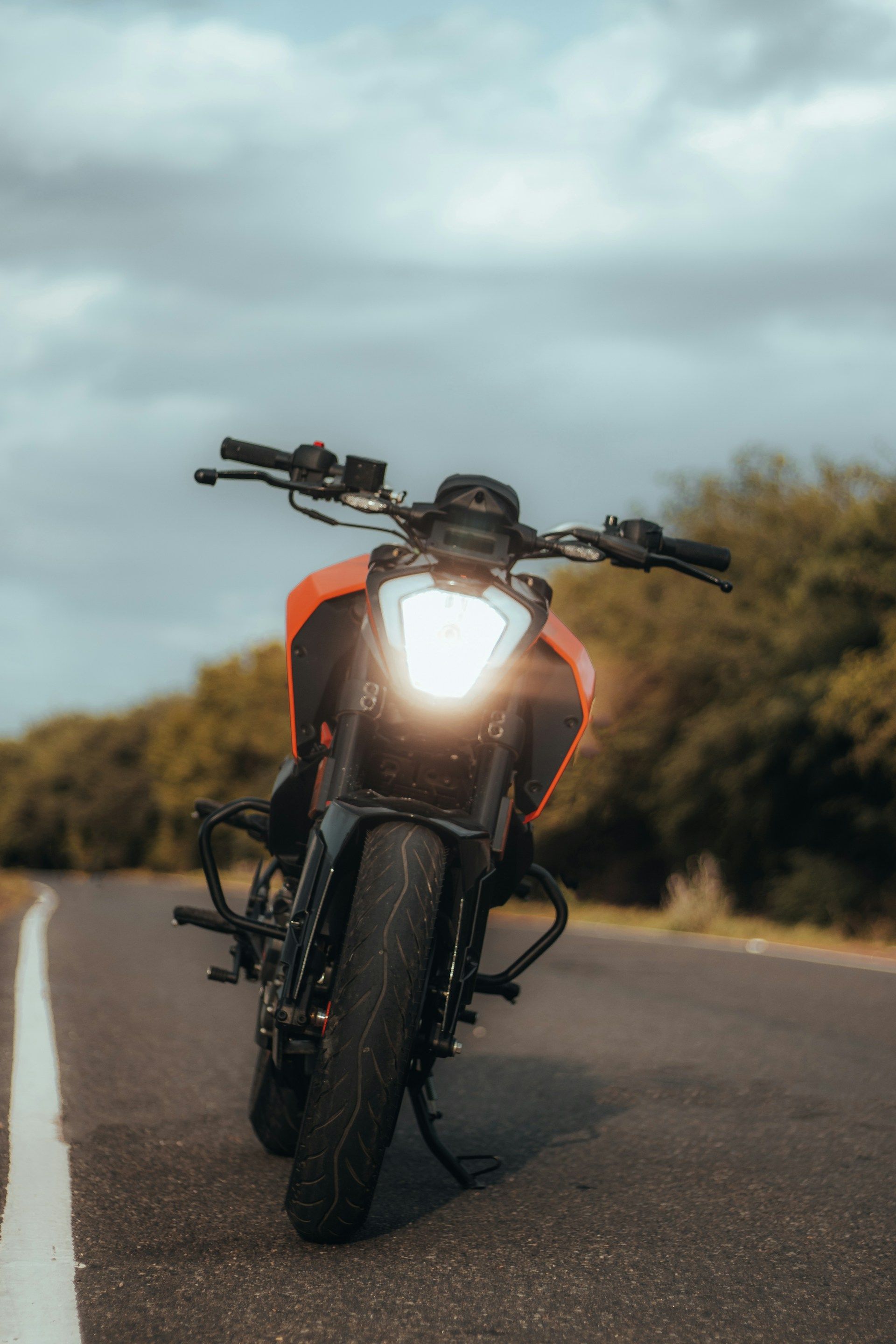 Orange motorcycle with bright headlight on a road under a cloudy sky