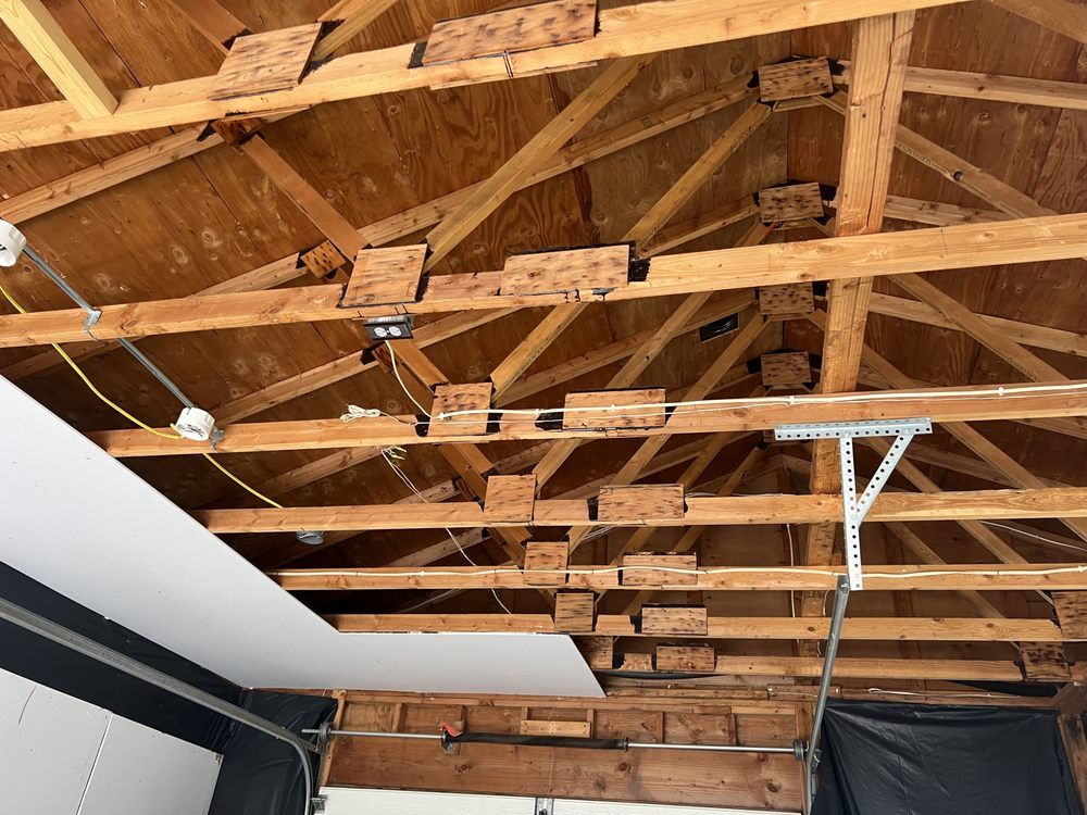 Exposed wooden roof trusses and rafters inside a room under construction with a strip of drywall below