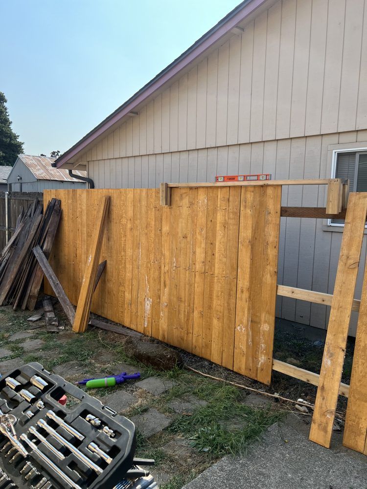 Wooden fence panels leaning against a beige building in a yard with construction materials scattered nearby