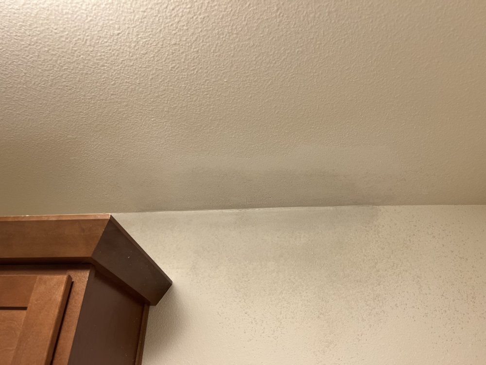 Corner of a room with a beige wall and the top of a wooden cabinet on the left.