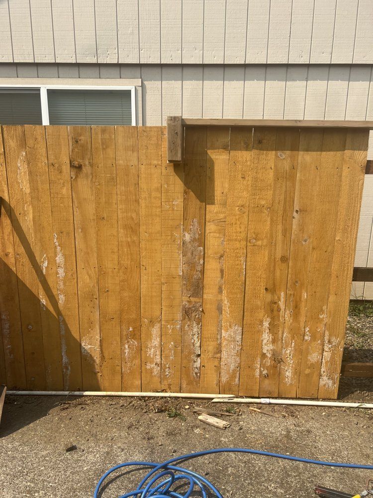 Weathered wooden fence beside a house wall, with a gravel ground and blue hose in front.