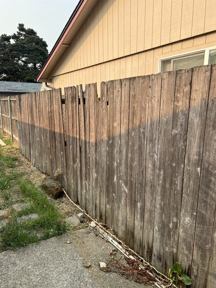 Weathered wooden fence beside a tan house along a cracked sidewalk