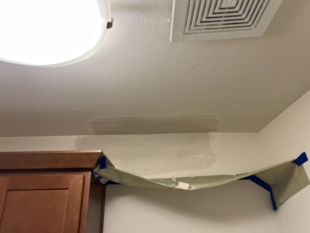 Ceiling patch near a cabinet, with taped plastic draped across a damaged section.