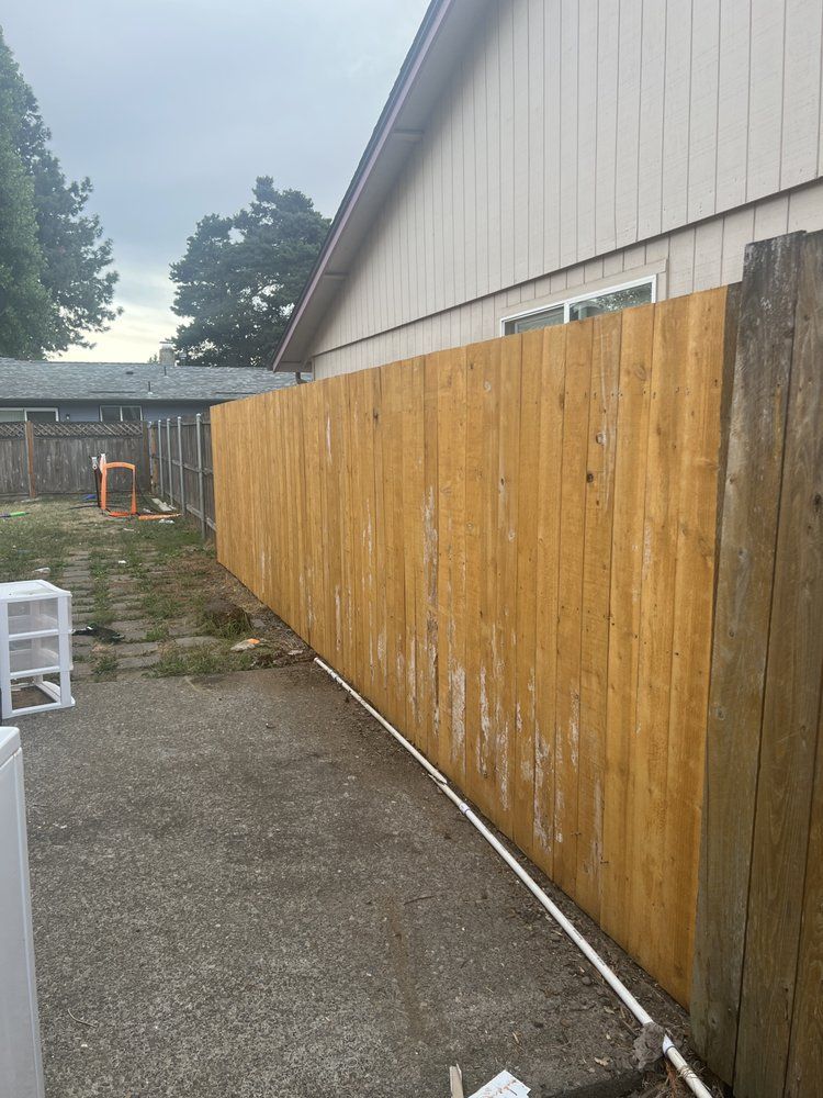Long wooden fence along a gravel side yard beside a beige building under a cloudy sky