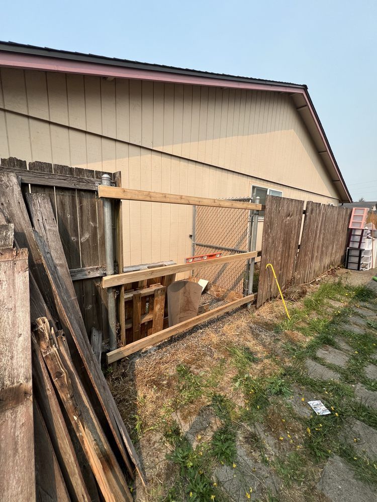 Makeshift wooden fence and gate along a tan building beside a dirt path