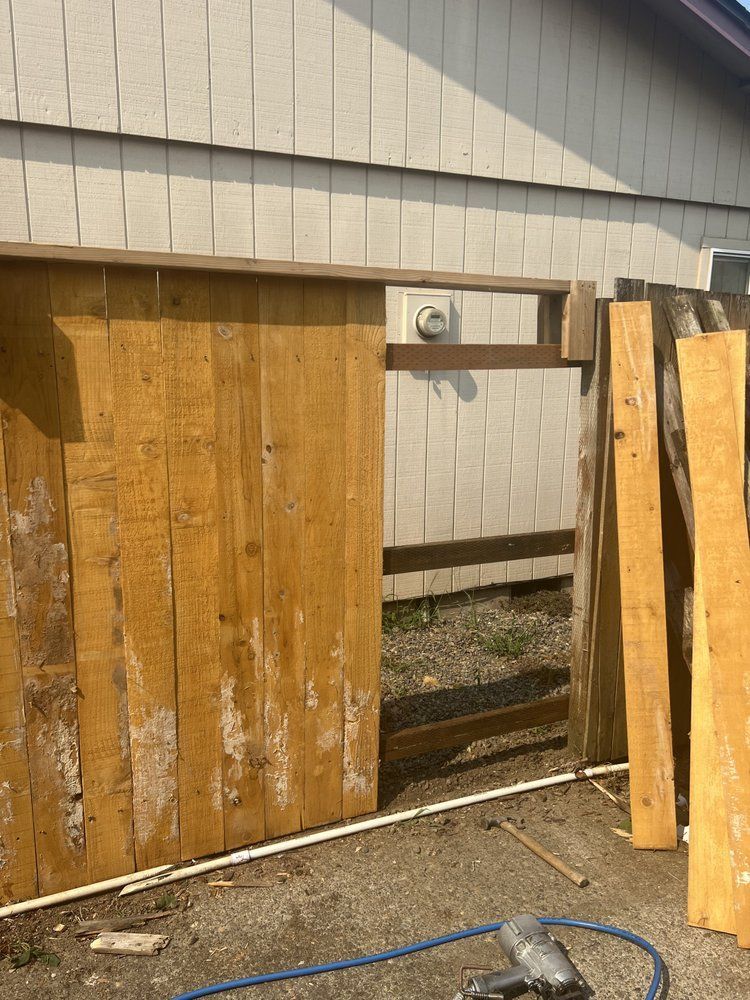 Wooden fence gate opening under a house wall with a small metal latch and gravel ground nearby