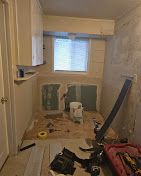 Small bathroom under renovation with exposed wall studs, window, toilet, and tools on the floor