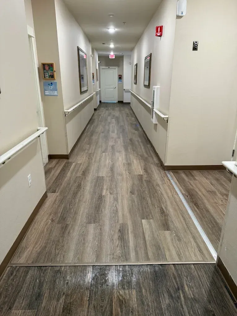 Empty beige hallway with wood-pattern flooring, handrails, and exit signs.