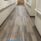 Empty hallway with beige walls, white handrails, and gray wood flooring leading to a door at the end