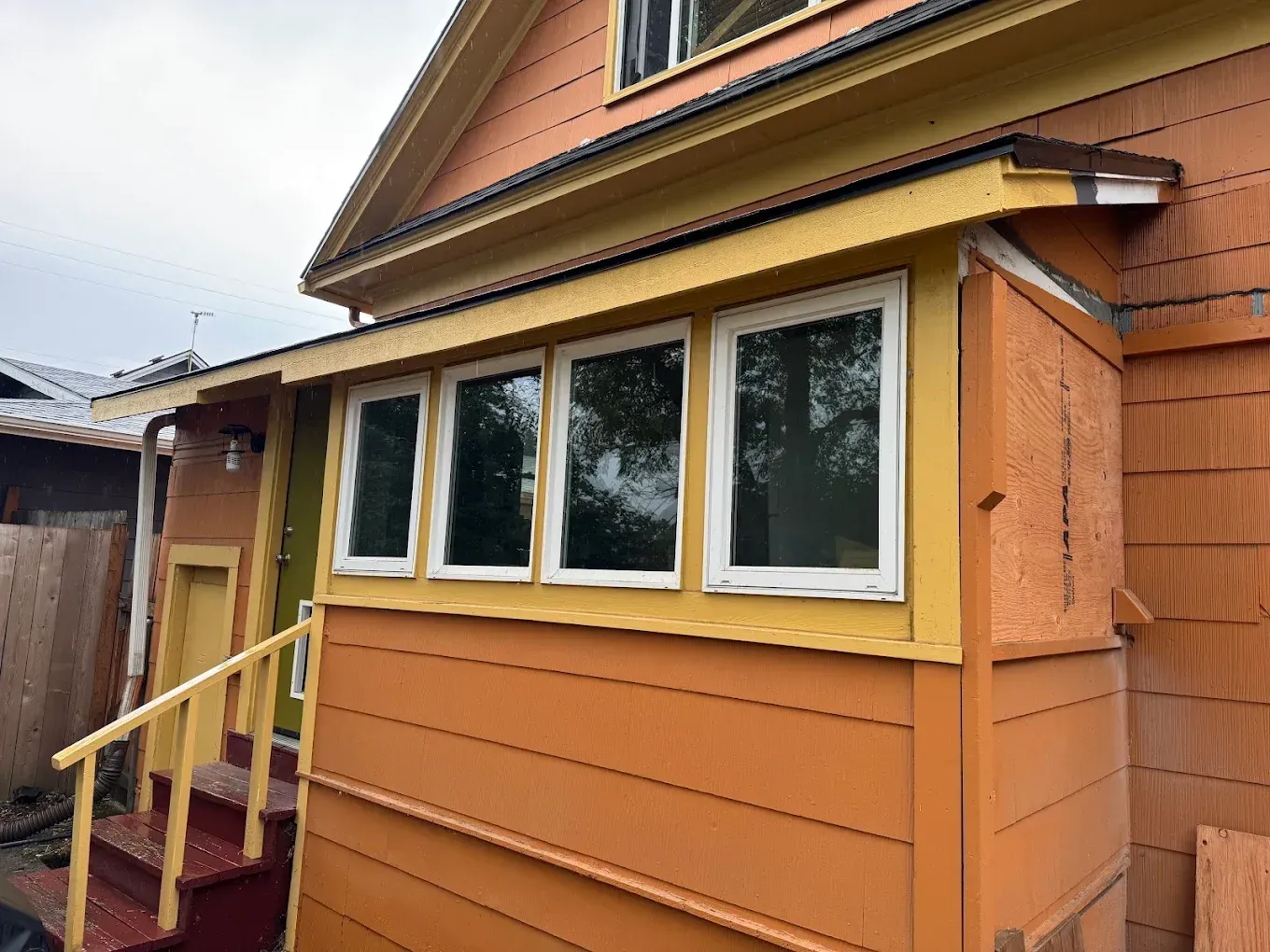 Wooden house exterior with cream-trimmed windows and a yellow-railed porch stairway