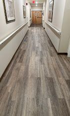 Empty hallway with wood-look flooring, white walls, framed pictures, and a wooden door at the end.